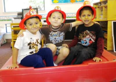 3 young boys with firemen hats in classroom