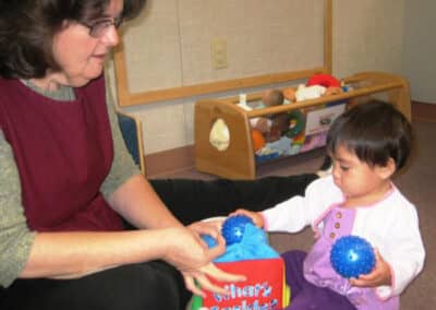 Staffer with baby girl playing with plastic balls.