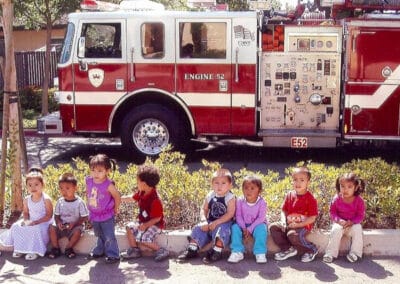 Small children sitting on a curb in front of a fire engine on a field trip.