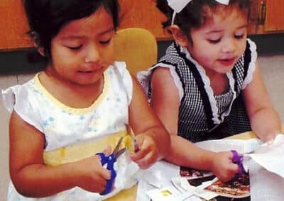 Two little girls cutting paper for a craft.